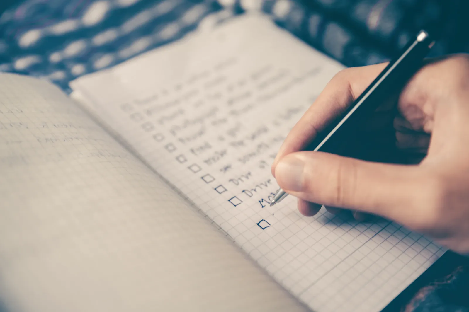 A hand holding a pen over a handwritten checklist in a notebook.