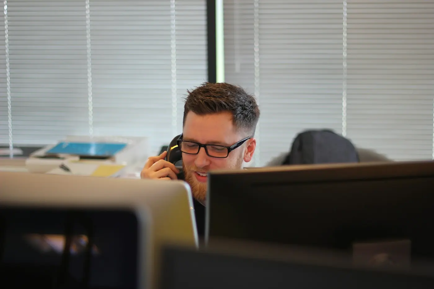 Person speaking on an office phone behind computer monitors.