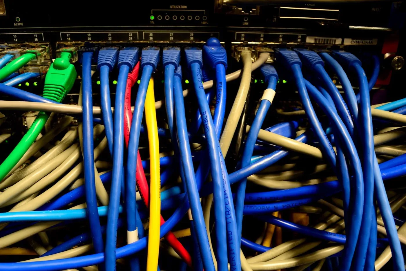 The back of a network switch with a row of numbered ports and an activity meter, connected to a dense tangle of blue, grey, green, red and yellow ethernet cables.