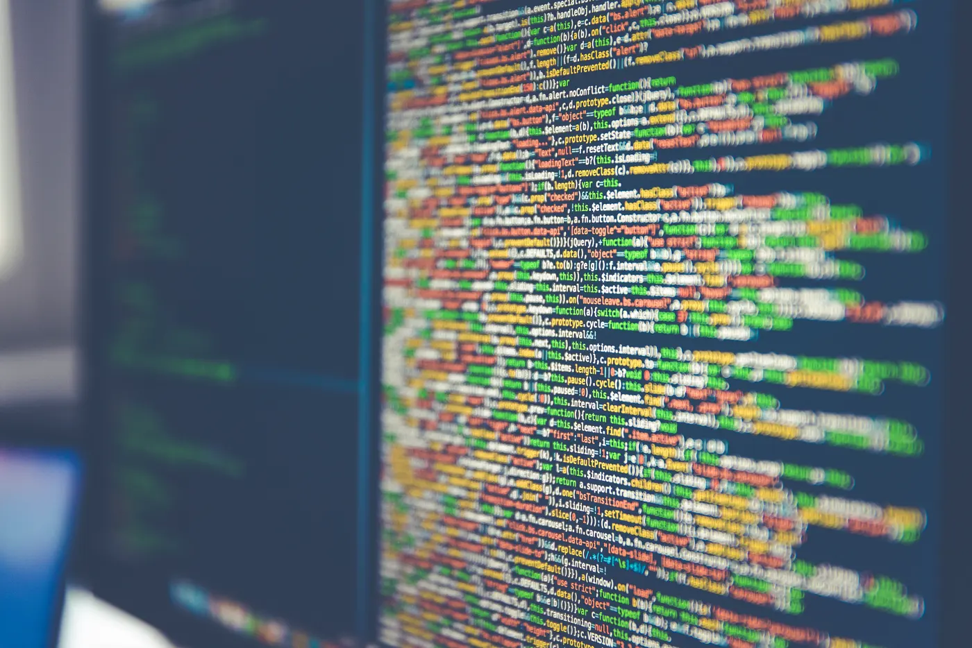 Lines of colour-highlighted, minified JavaScript code on a dark computer monitor, photographed at an angle with a shallow depth of field.