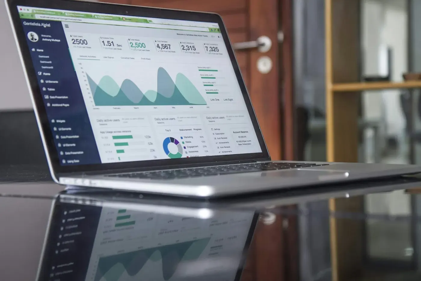Open laptop displaying charts on a glass table.