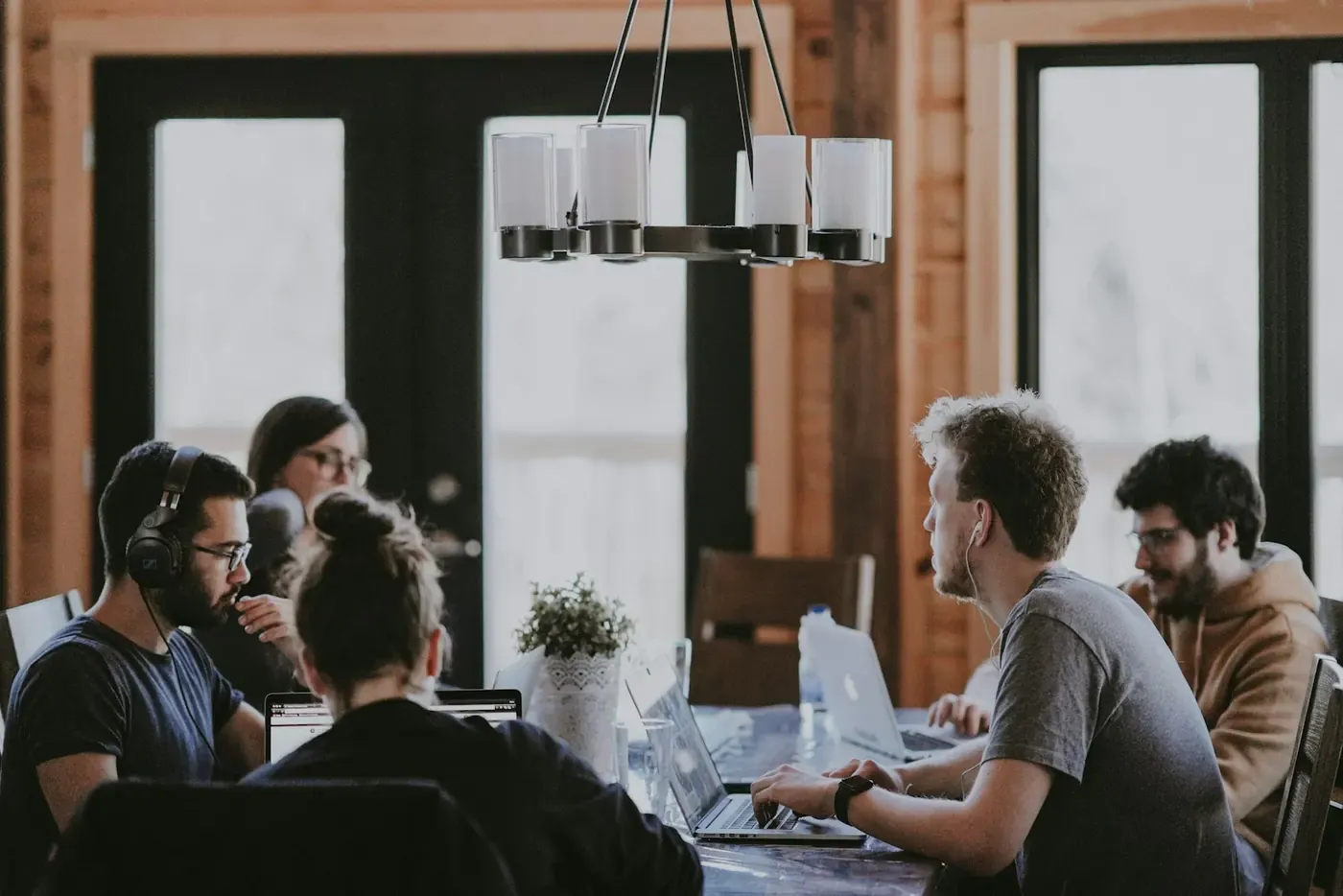 People in conversation around a table with laptops in a timber-lined studio.