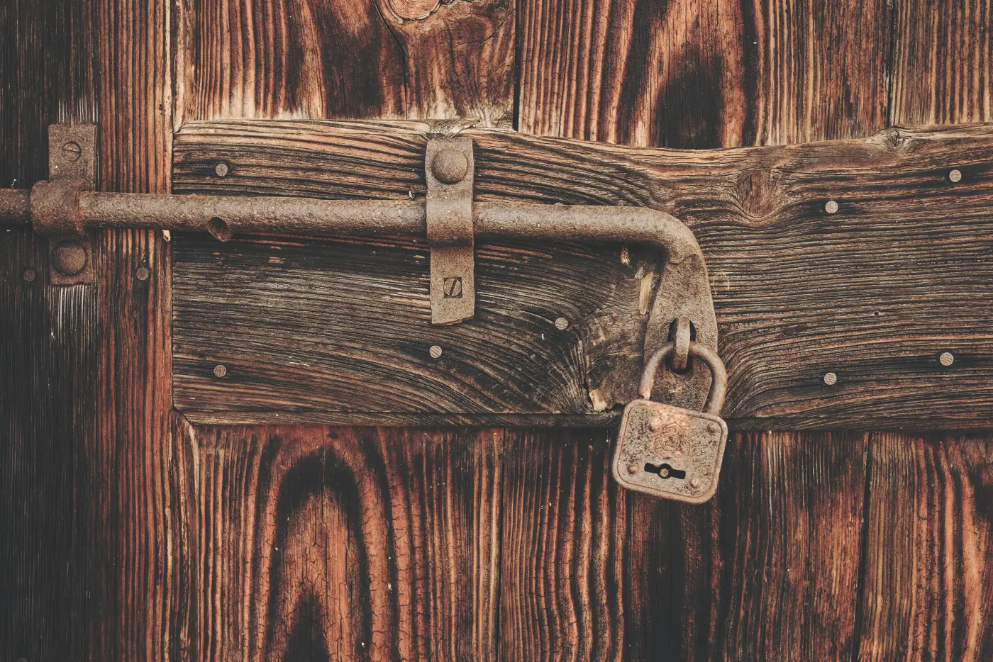 A rusty iron bolt slid across an old timber door and fastened with a small rusted padlock.