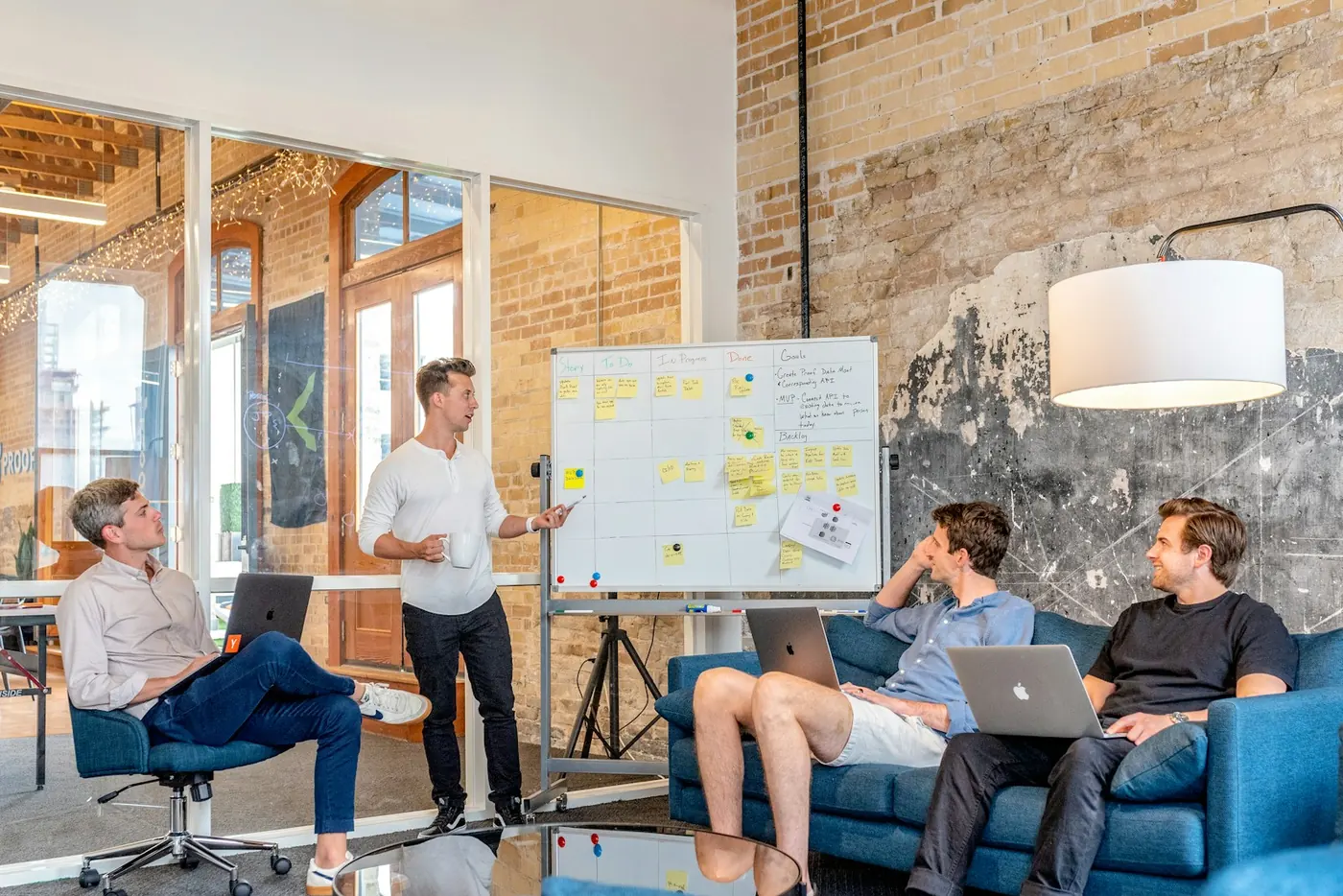 Small group watching a presentation beside a whiteboard in a brick-walled office.