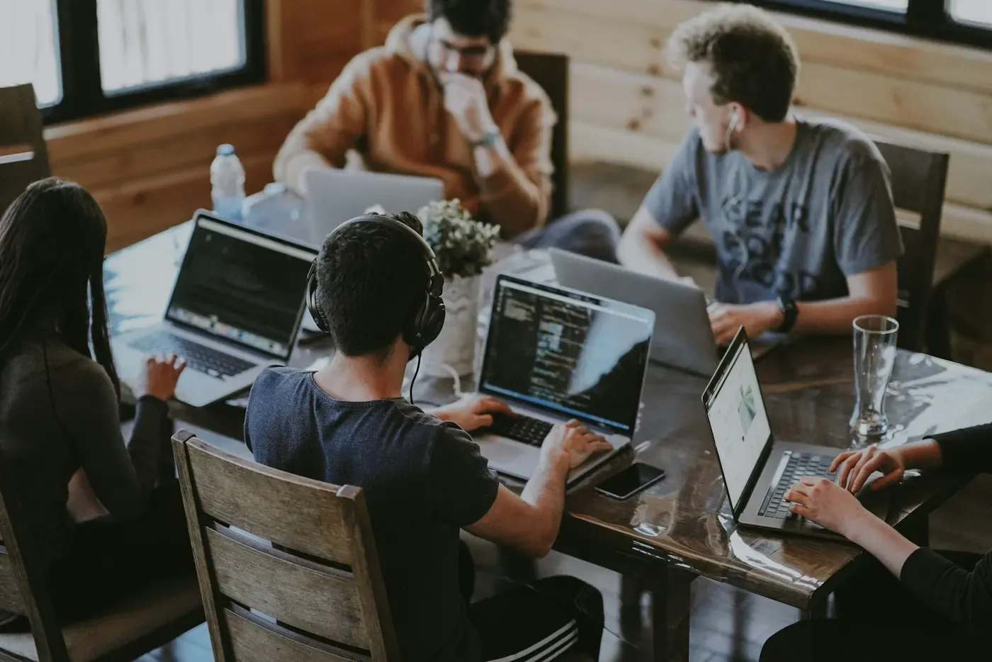 People collaborating at a table with open laptops in a timber-lined studio.