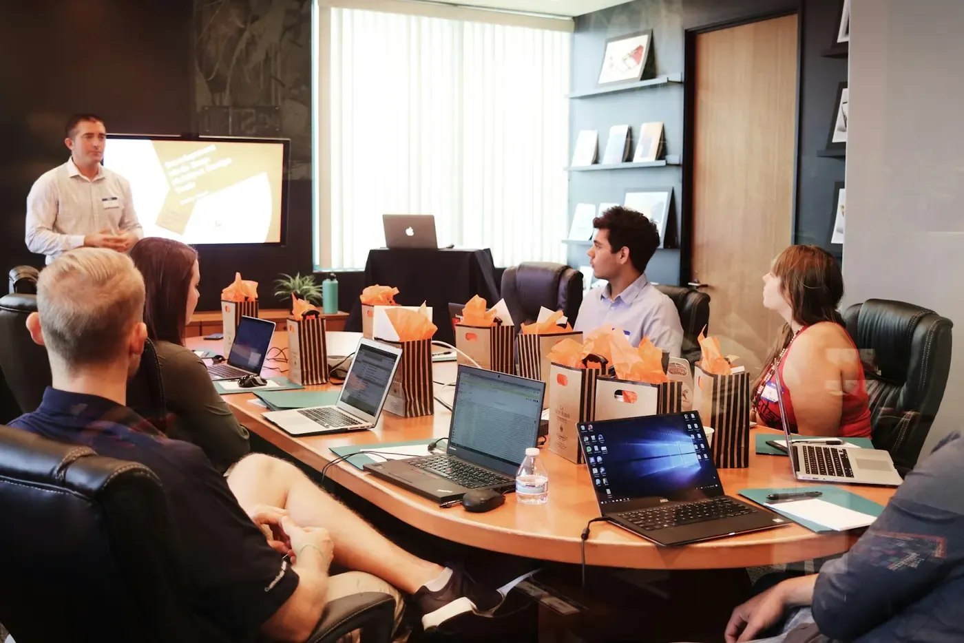 People meeting around a table while a presenter stands beside a screen.