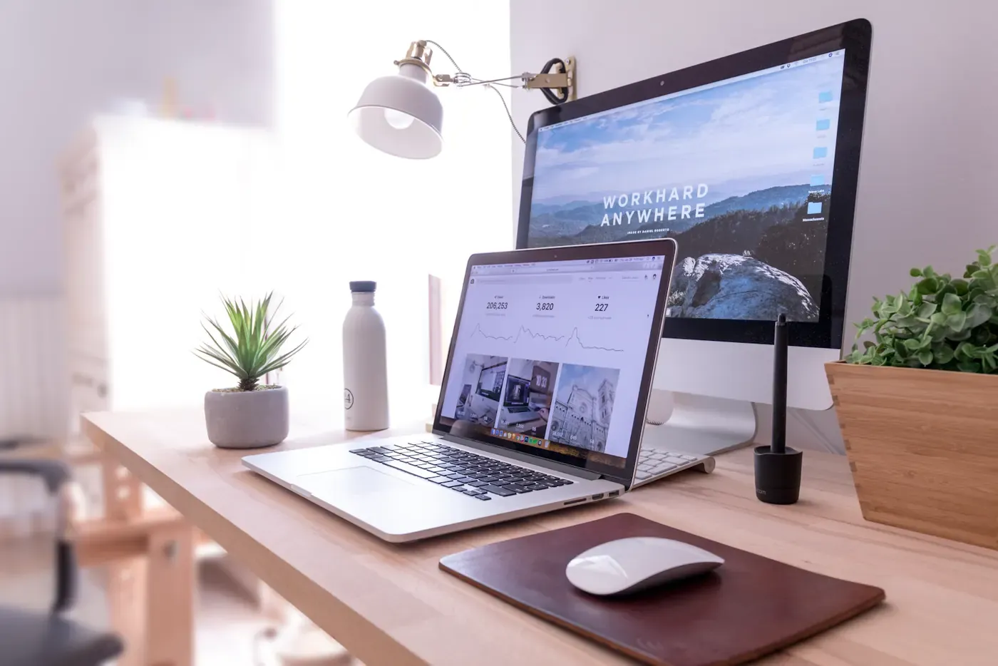 Laptop and desktop monitor on a bright desk with plants.